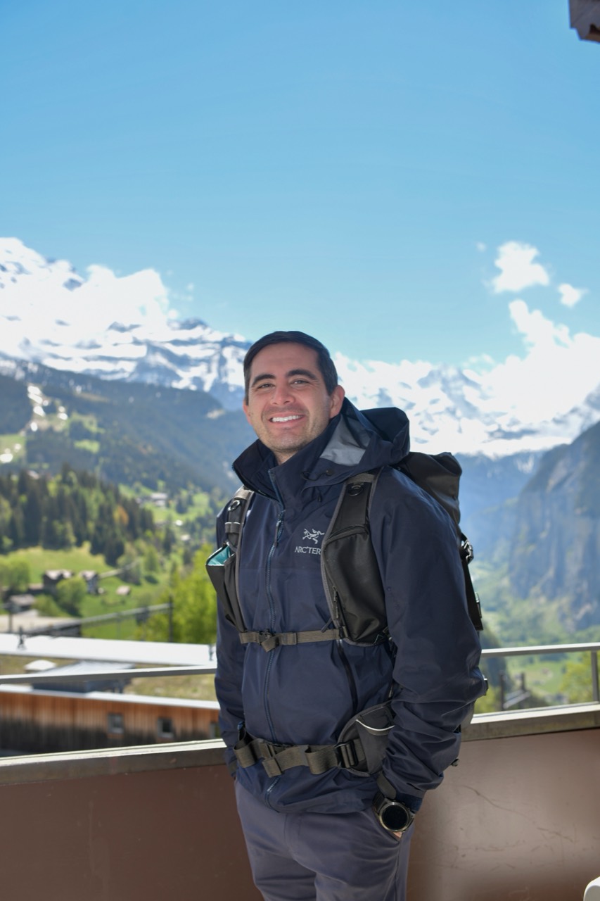 Reed Cameron Osaki wearing a hiking backpack in front of a mountain landscape.